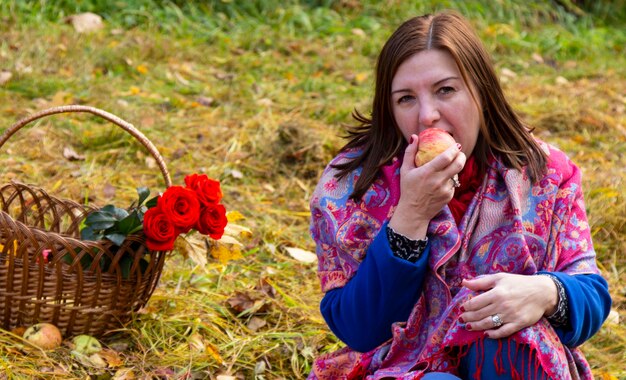 Een vrouw bijt een appel tijdens een picknick in het park. Mand met rozen, appels in het herfstpark.