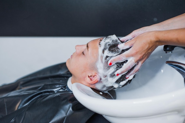 Een vrouw brengt shampoo aan en masseert het haar van een klant De man wast zijn haar in de kapperszaak