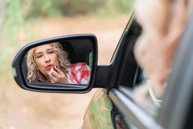 Een vrouw die achter het stuur van een auto zit, schildert haar lippen terwijl ze in de zijspiegel kijkt