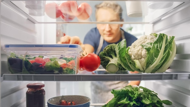 Een vrouw die door een koelkast vol eten kijkt