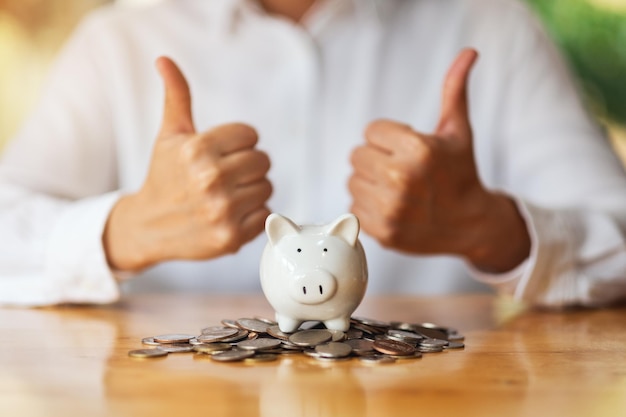 Een vrouw die duimen omhoog handtekent en laat zien met munten en spaarvarken op tafel om geld te besparen concept