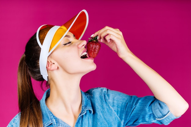 Een vrouw die een aardbei eet op een roze achtergrond