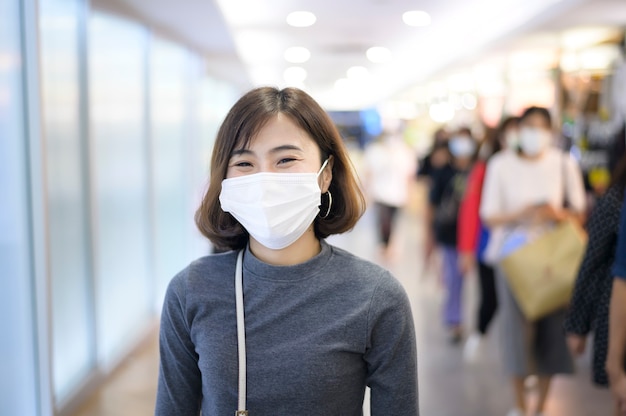 Een vrouw die een beschermend masker draagt, winkelt onder Covid-19 pandemie in een winkelcentrum, sociaal afstandsprotocol, nieuw normaal concept.