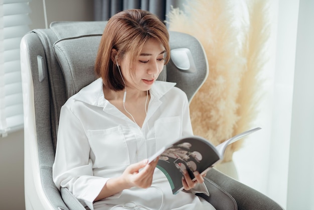 Een vrouw die een boek leest en naar muziek luistert terwijl ze op de massagestoel in de woonkamer zit