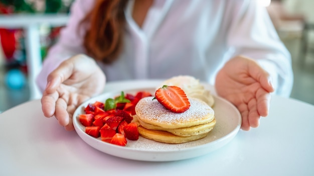 Een vrouw die een bord pannenkoeken met aardbeien en slagroom vasthoudt en toont