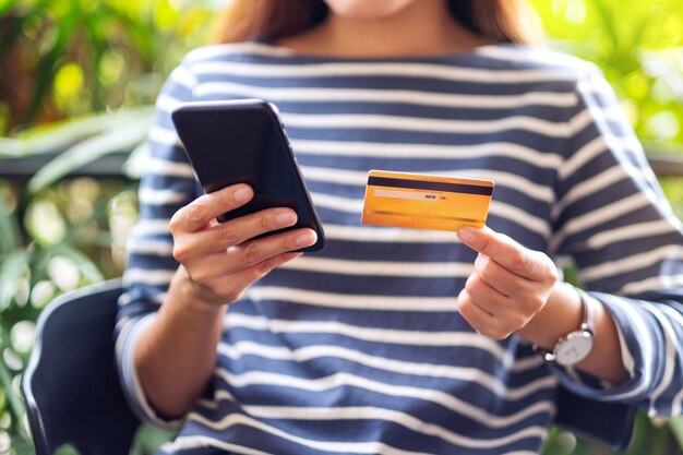 Een vrouw die een creditcard vasthoudt en naar een mobiele telefoon wijst om online te kopen en te winkelen