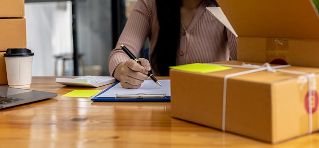 Een vrouw die een e-commercebedrijf runt, schrijft een lijst met klanten op papier voordat ze naar hen verzendt, ze runt een e-commercebedrijf op websites en sociale media. Concept van het online verkopen van producten.