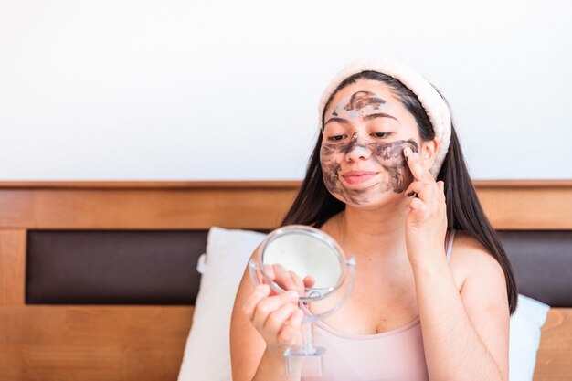 Een vrouw die een gezichtsmasker aanbrengt voor een spiegel.