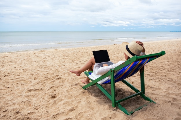 Een vrouw die een laptop gebruikt en typt terwijl ze op een strandstoel ligt