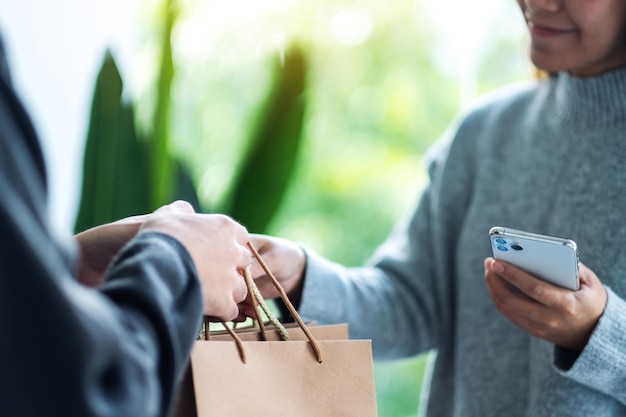 Foto een vrouw die een mobiele telefoon vasthoudt en boodschappentassen ontvangt van de bezorger