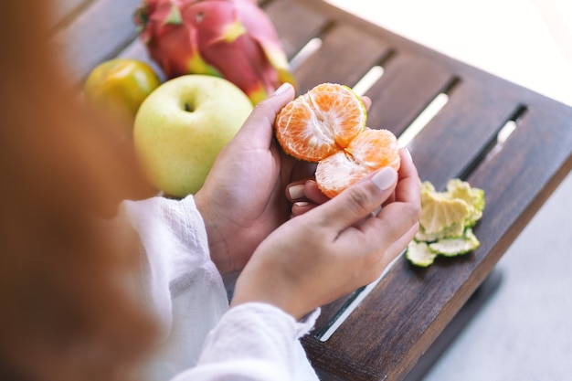 Een vrouw die een sinaasappel vasthoudt en pelt om te eten met peer en drakenfruit op een kleine houten tafel