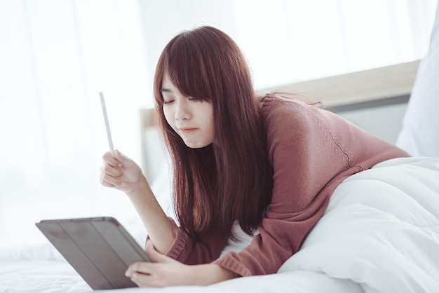 Een vrouw die een tablet speelt op het bed in een witte slaapkamer