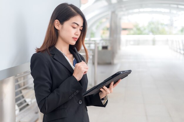 Een vrouw die een zwart pak draagt, kijkt peinzend naar de tablet.