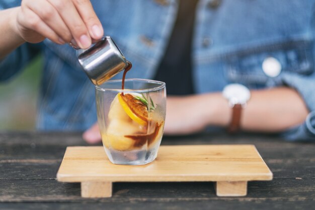 Een vrouw die espresso giet schoot in een glas ijs en citroen