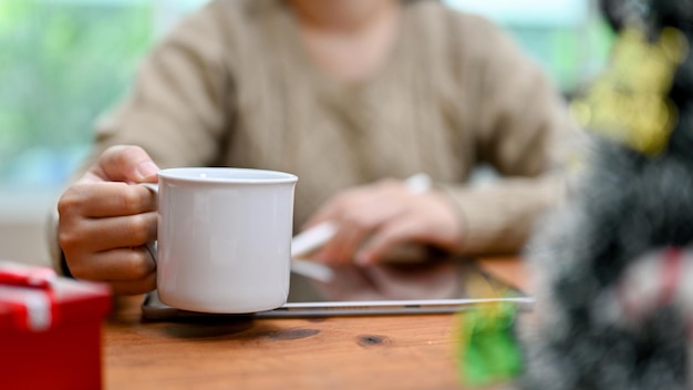 Foto een vrouw die koffie nipt terwijl ze een tablet gebruikt die thuis aan haar bureau werkt, heeft een bijgesneden opname gemaakt