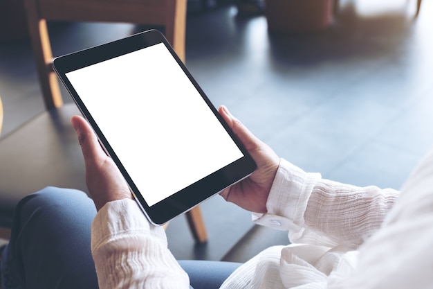 een vrouw die met gekruiste benen zit en zwarte tabletpc met het lege witte Desktopscherm houdt