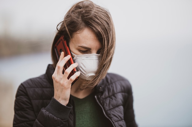 Een vrouw die op de telefoon met coronavirusmasker spreekt