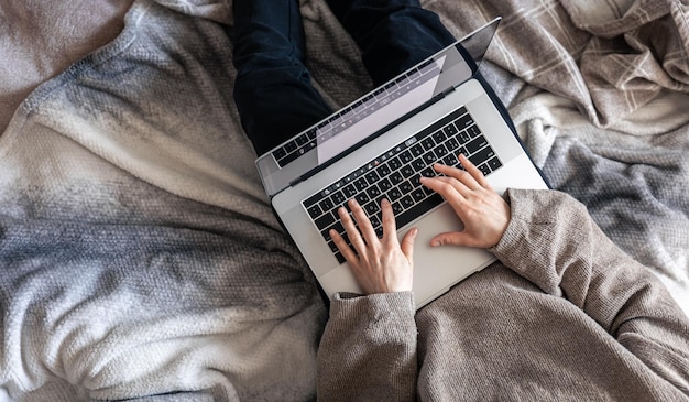 Een vrouw die op een laptop werkt terwijl ze in bed ligt bovenaanzicht