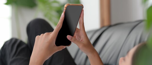 Een vrouw die op zwarte laag ligt en smartphone in woonkamer op vrije dag gebruikt