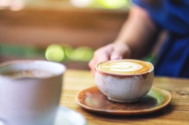 Een vrouw die 's ochtends een kop hete latte-koffie op een houten tafel houdt