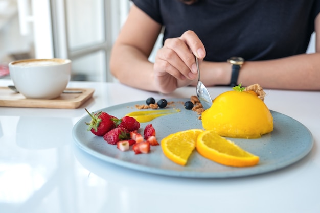 Een vrouw die sinaasappelcake met gemengd fruit eet door lepel in koffie