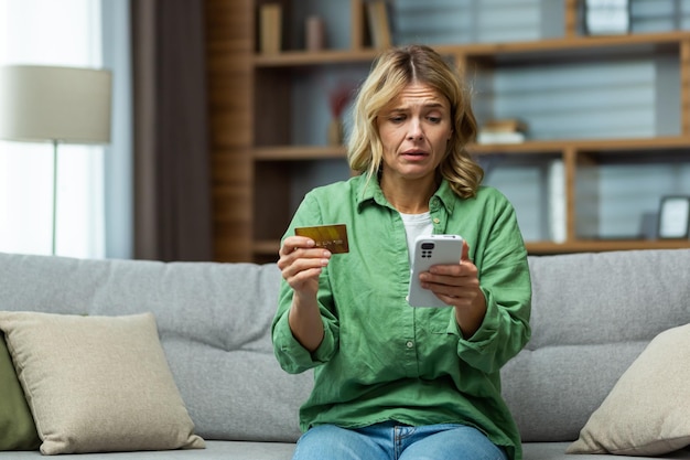 Een vrouw die thuis op de bank zit en bezorgd telefoon- en creditcardproblemen met de rekening vasthoudt