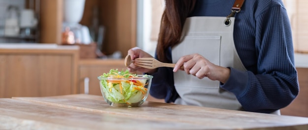 Een vrouw die thuis verse salade met gemengde groenten kookt en eet