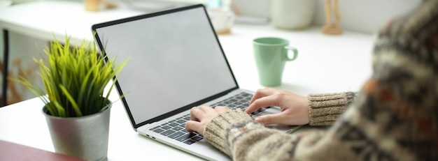 Een vrouw die werkt op een leeg scherm laptop met koffiemok en decoratie op eenvoudige werktafel