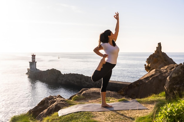 Een vrouw die yoga-oefeningen doet in de natuur aan zee dandayamana dhanurasana