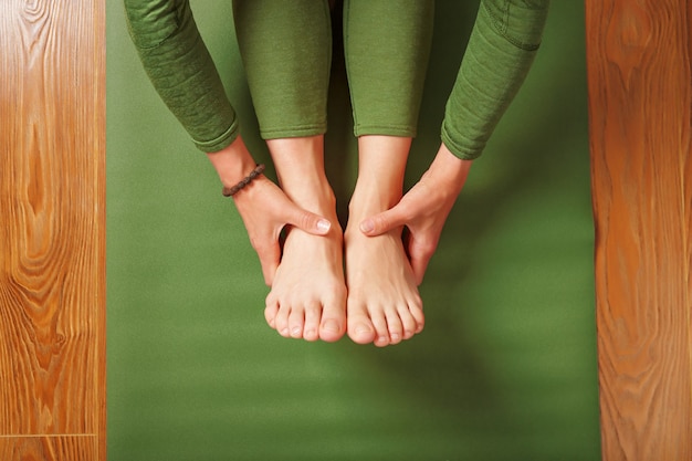 Een vrouw doet yoga op een groen tapijt thuis in de woonkamer. Asana's in Hatha yoga, fitness en thuis sporten.