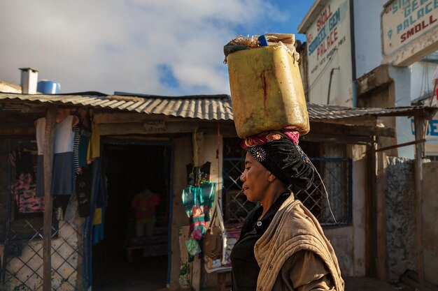Een vrouw draagt een plastic emmer met goederen op haar hoofd. Madagascar