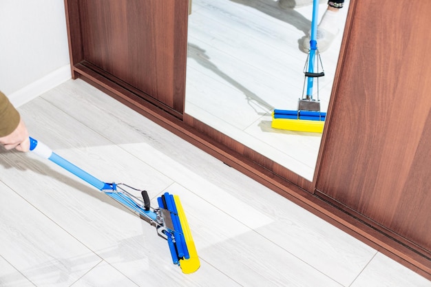 Een vrouw dweilt de vloer in de kamer weerspiegeld in de gespiegelde kastdeur Schoonmaken in huis