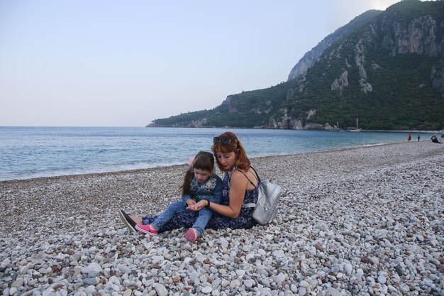 een vrouw en een kind zitten op een strand een van hen houdt een rugzak vast