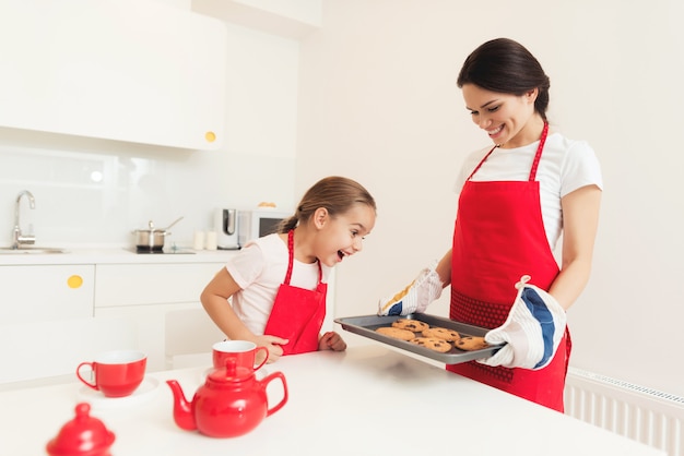 Een vrouw en een meisje in rode schorten bakken koekjes en muffins