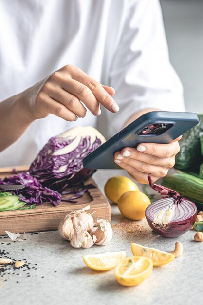Een vrouw gebruikt een smartphone in de keuken tijdens het bereiden van een groente salade