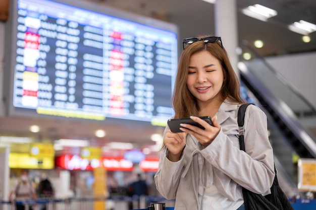 Een vrouw gebruikt haar smartphone om de tijd van haar boarding te controleren terwijl ze op de luchthaven staat