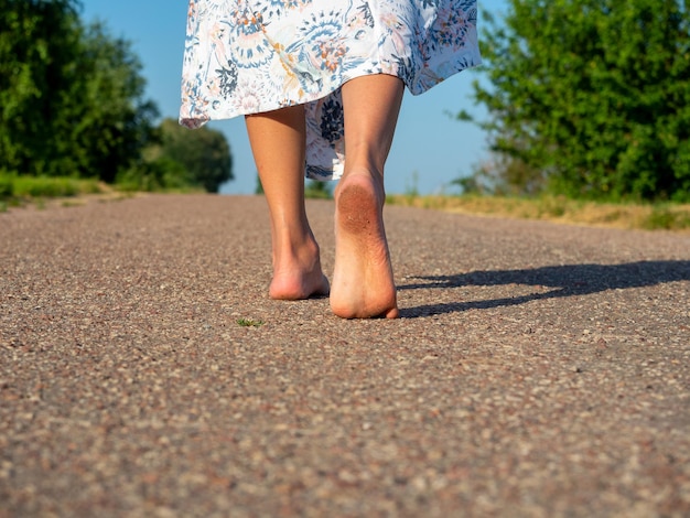 Een vrouw gekleed in een jurk loopt blootsvoets op het asfalt. Achteraanzicht. Het concept van reizen, recreatie, vakantie, vrijheid