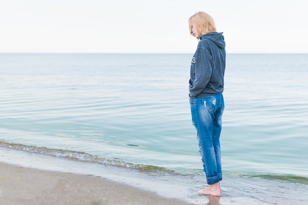 Een vrouw gekleed in jeans en een trui staat aan de kust in het water Concept Women's eenzaamheid depressie