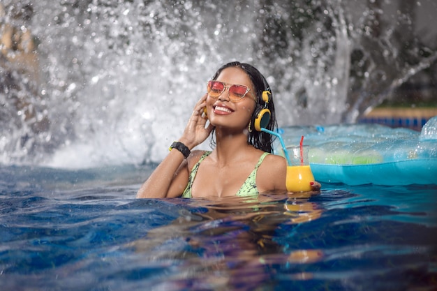 een vrouw geniet in een zwembad met een cocktail in haar hand.