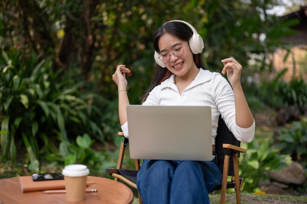 Een vrouw geniet van de muziek op haar koptelefoon terwijl ze aan haar laptop werkt in haar achtertuin