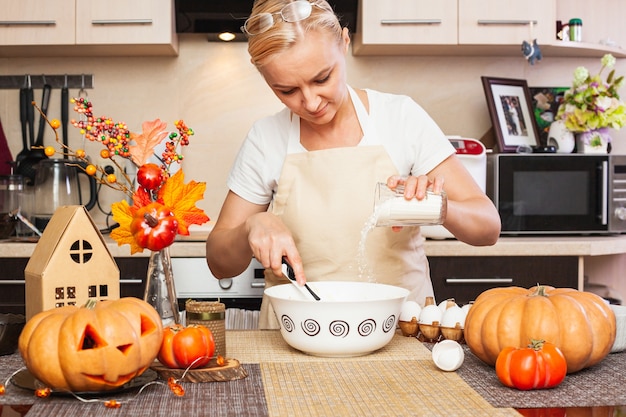 Een vrouw giet bloem in koekjesdeeg voor Halloween in de keuken met een herfstdecor. Gezellig huis en voorbereiding, koekjes maken voor Halloween.