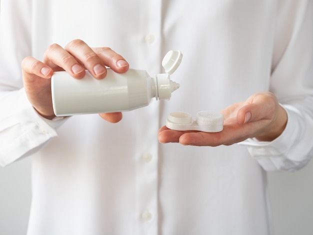 Een vrouw giet een contactlensoplossing in een contactlenscontainer.