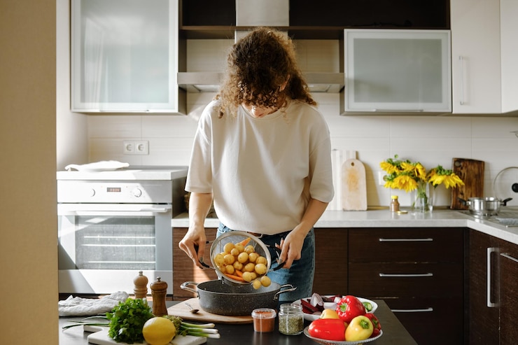 Foto een vrouw giet gekookte aardappelen en wortels uit een colander in een pan