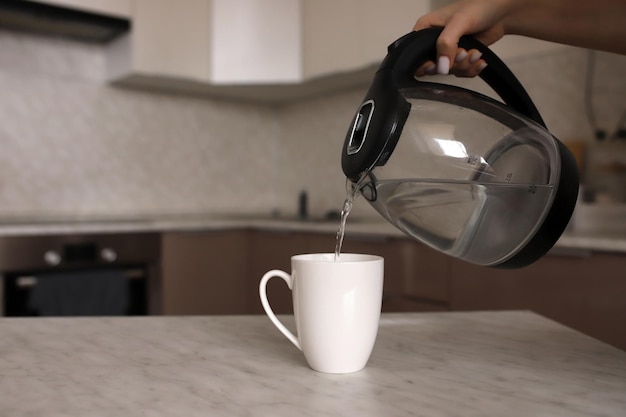 Een vrouw giet kokend water in een witte mok op de keukentafel