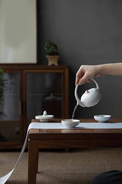 Een vrouw giet thee in een theepot op een tafel Rustig thee drinken in de ochtend