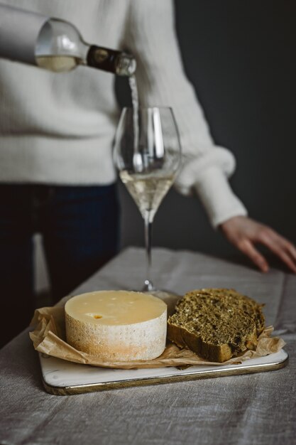 Een vrouw gieten een glas witte wijn uit een fles, kaas en brood op een snijplank. Verticale levensstijlfoto