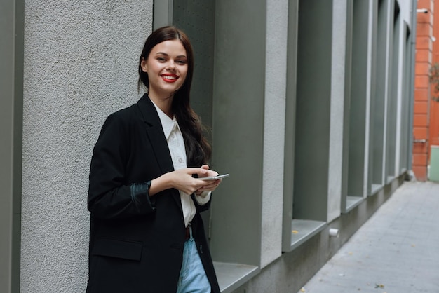 Een vrouw glimlacht met tanden met een telefoon in haar handen loopt door de stad mode op straat voorjaarsvakantie vakantie in de stad toeristische freelancer mobiele communicatie en internet
