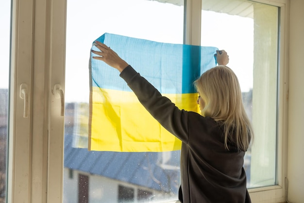 Een vrouw hangt een vlag van oekraïne aan het raam