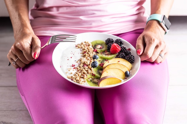 Een vrouw heeft een gezond ontbijt na ochtendgymnastiek yoghurt bramen muesli frambozen enz.