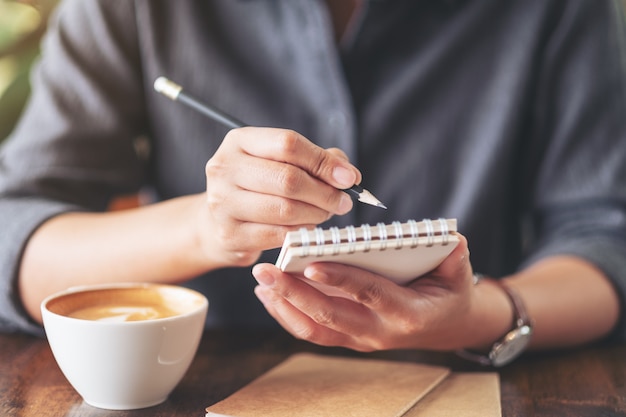 Een vrouw houden en schrijven op blanco notebook met koffiekopje op houten tafel